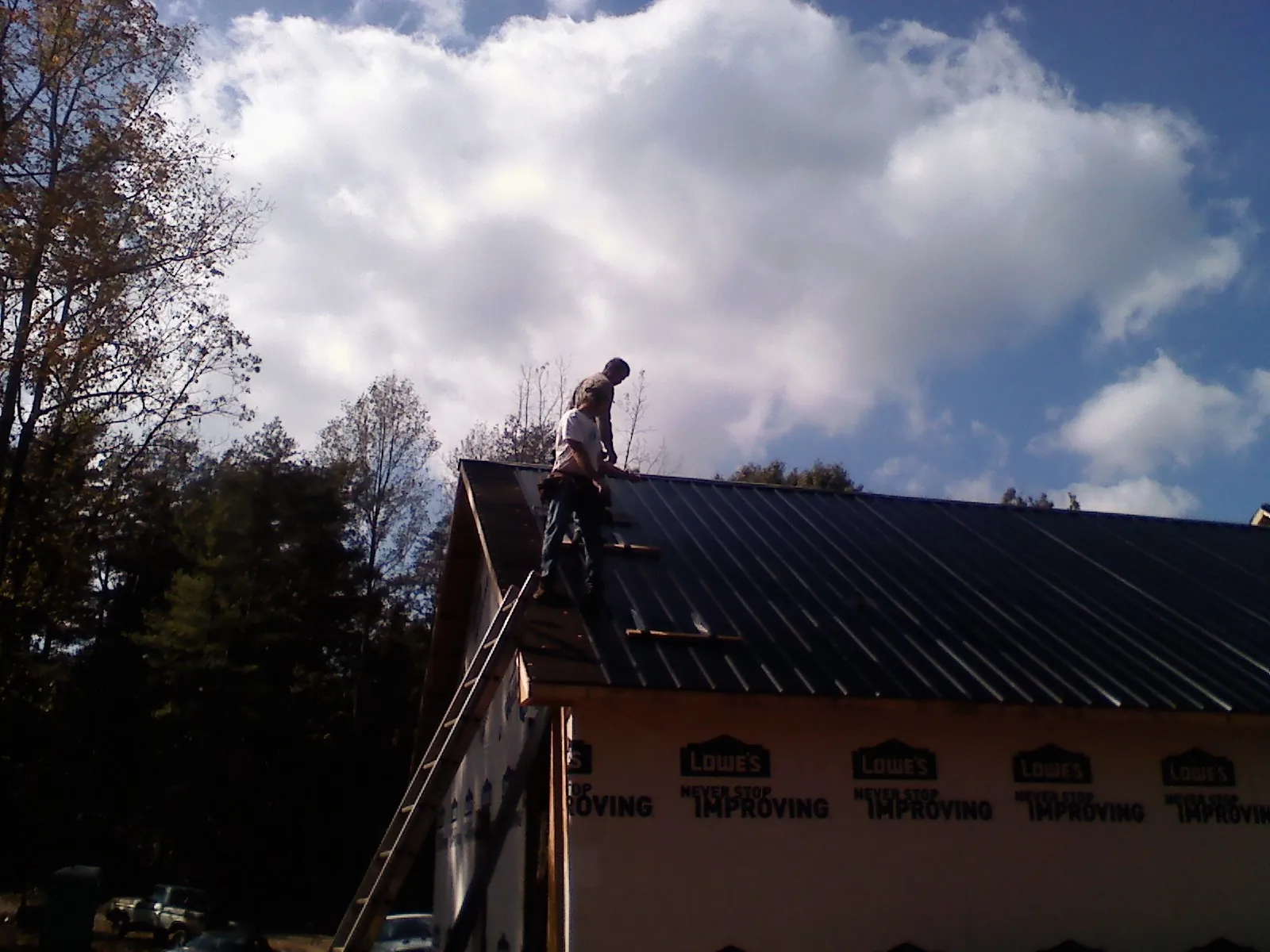 Roofer fastening dark metal panels high against a cloudy sky, from a Roof Inspection job in Cassville
