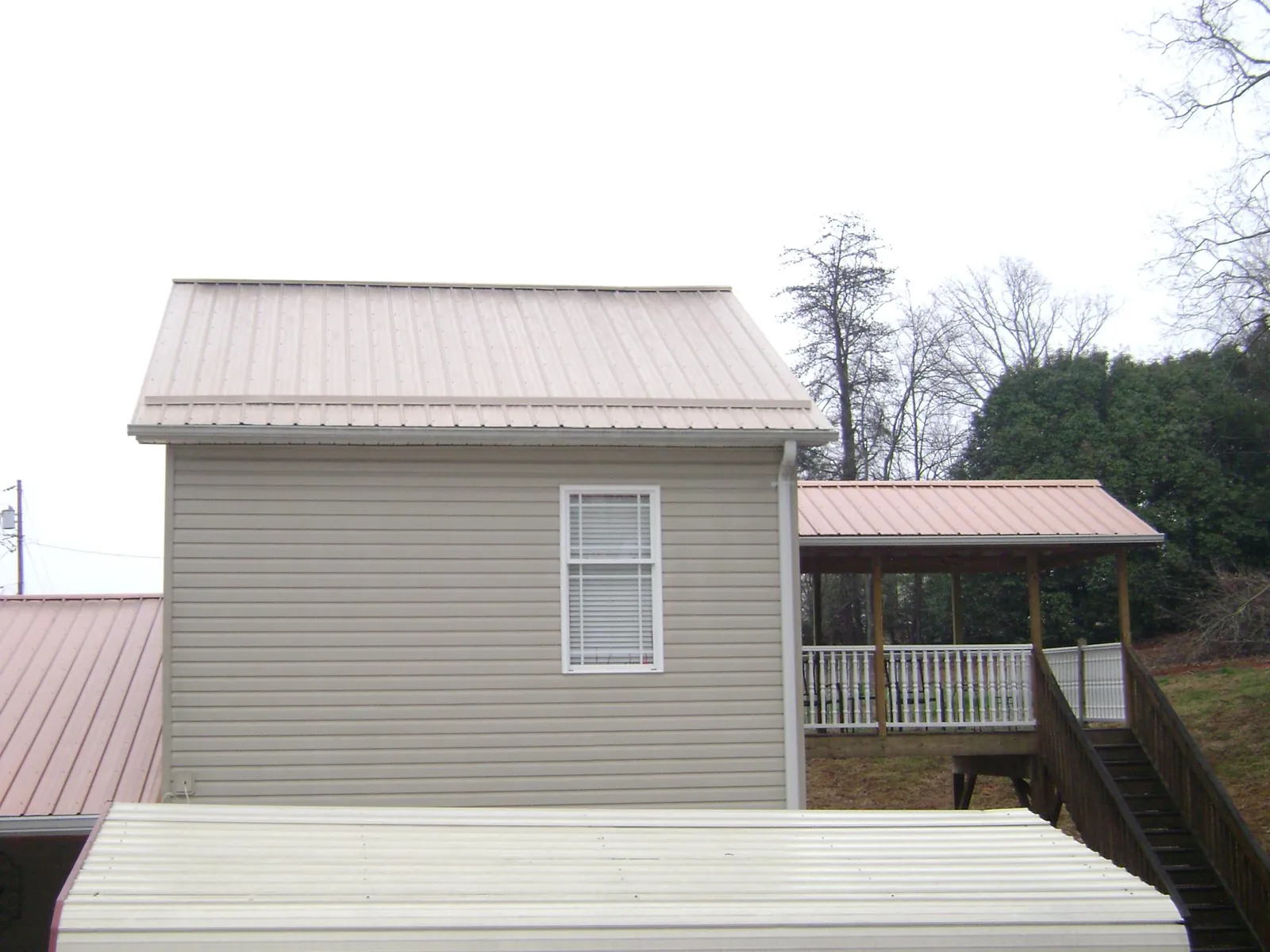 Tan metal roofs on a two story addition and attached porch, from a Roof Replacement job in Cassville